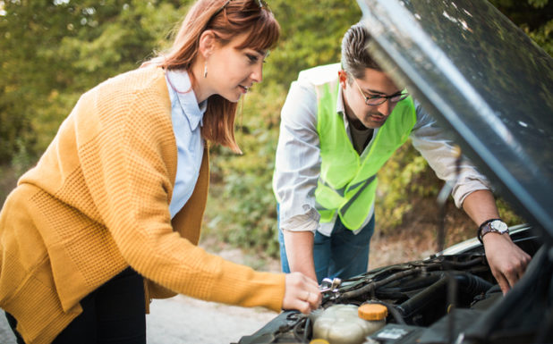 Man in a safety vest and a woman in a sweater looking under the hood of a vehicle.