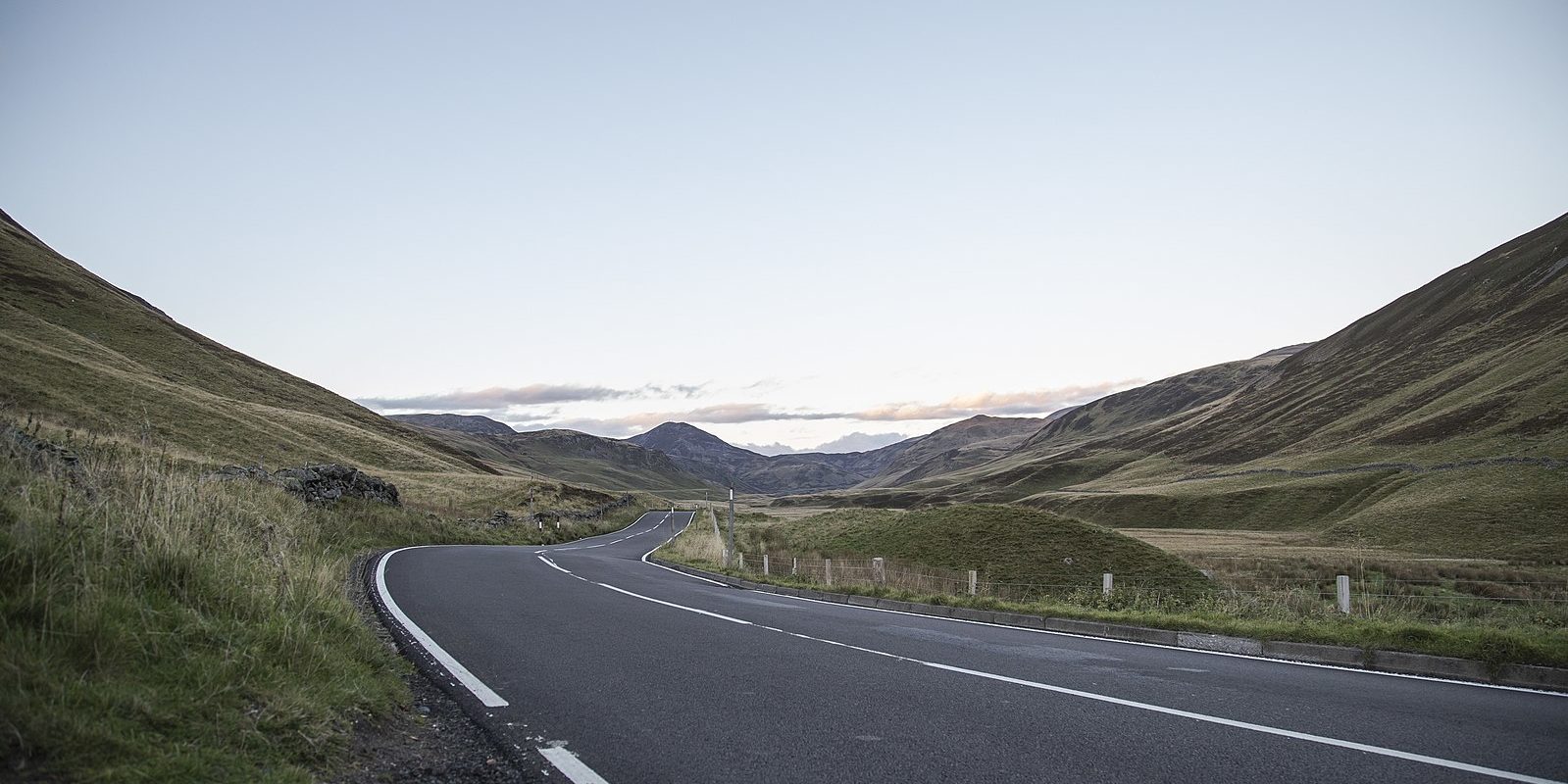 Photograph of an empty road winding through a shallow mountain valley.