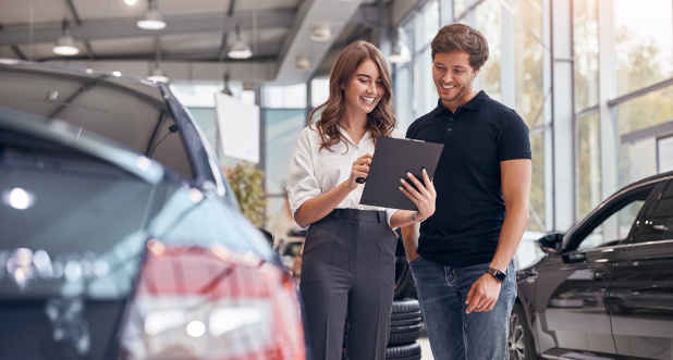 Smiling car dealer employee presenting warranty paperwork to pleased customer at certified dealership