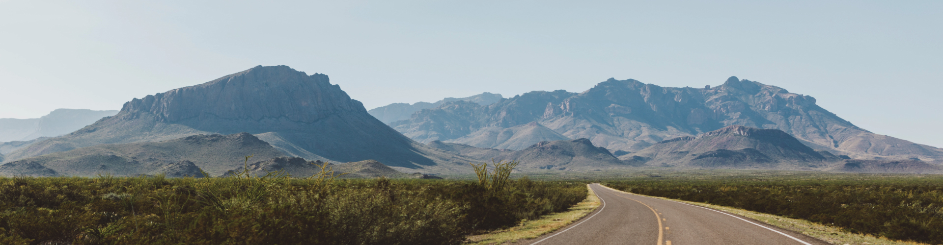 Photo of a road in a semi-arid plain leading into far-off mountains.